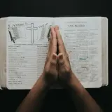 Dłonie złożone w modlitwie nad otwartą Biblią, w której widnieje porównanie Starego i Nowego Testamentu. To chwila refleksji i psalmy uwielbienia.