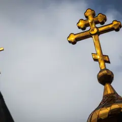 Złoty krzyż prawosławny na tle pochmurnego nieba. Drugi krzyż prawosławny widoczny w oddali.