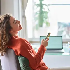 Kobieta z kręconymi włosami śmieje się, trzymając telefon. Czy 3 maja można pracować? Ona chyba odpoczywa.