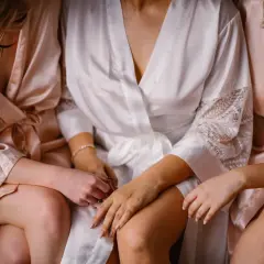 Trzy kobiety w satynowych szlafrokach, jedna w białym, dwie w pudrowym różu, siedzą blisko siebie. Delikatne dłonie spoczywają na kolanach. To idealny moment na panience na dobranoc tekst.