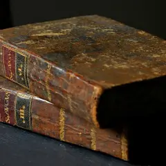 Dwie stare, skórzane księgi, jedna na drugiej. Na grzbietach widoczne etykiety z łacińskimi napisami, sugerujące zawartość, być może psalm 98.