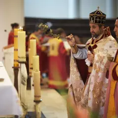 Dwaj duchowni w szatach liturgicznych podczas nabożeństwa, jeden z kadzielnicą, obok świece.
