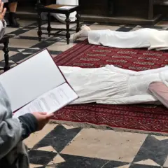 Dwie kobiety w białych sukniach leżą na dywanie w kościele. To uroczystość, podczas której zostają dziewicami konsekrowanymi.