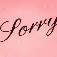 Napis "Sorry" czarną, ozdobną czcionką na różowym, chropowatym tle.