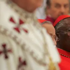 Kardynał w czerwonej szacie i okularach, obok duchowny w białej szacie z krzyżami.