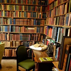Wnętrze biblioteki z regałami pełnymi książek. Na biurku leży poduszka z książkami, a obok krzesło. Nawet niewierzący doceniłby bogactwo wiedzy.
