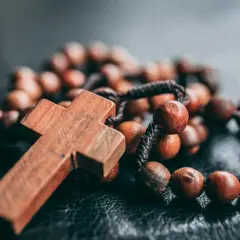 Drewniany różaniec z krzyżem na ciemnym tle.