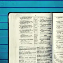 Otwarta Biblia z tekstem w języku angielskim na tle niebieskich desek.