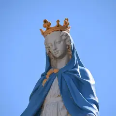 Figura Matki Bożej z koroną na głowie, w niebieskim płaszczu. Jej postawa przypomina błogosławieństwo z Psalmu 112.