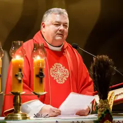 Ksiądz w czerwonej dalmatyce czyta tekst przy świecach. 24 marca, w kościele panuje uroczysta atmosfera.