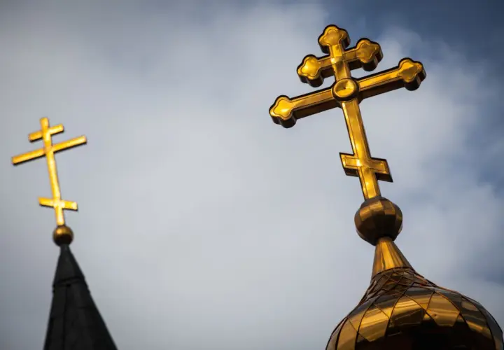 Złoty krzyż prawosławny na tle pochmurnego nieba. Drugi krzyż prawosławny widoczny w oddali.