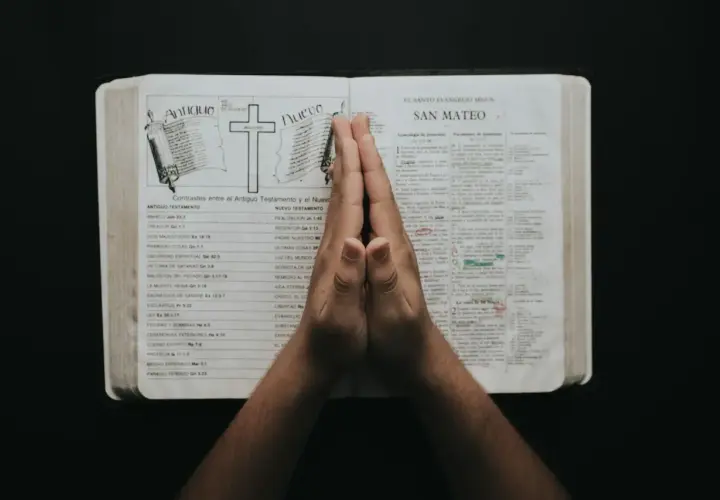Dłonie złożone w modlitwie nad otwartą Biblią, w której widnieje porównanie Starego i Nowego Testamentu. To chwila refleksji i psalmy uwielbienia.