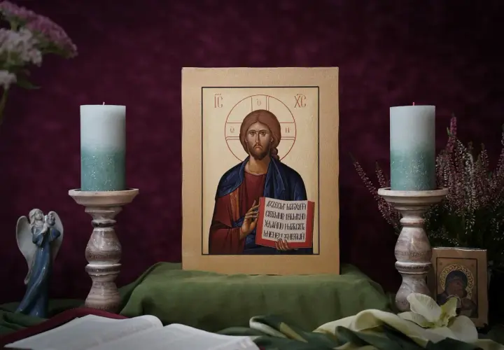 Ikona Chrystusa Pantokratora, otoczona świecami i kwiatami, emanuje spokojem.
