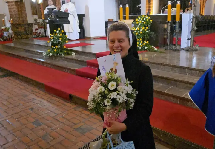 Radosna zakonnica z bukietem kwiatów i kartką z nutami. W tle msza święta, 25 października.