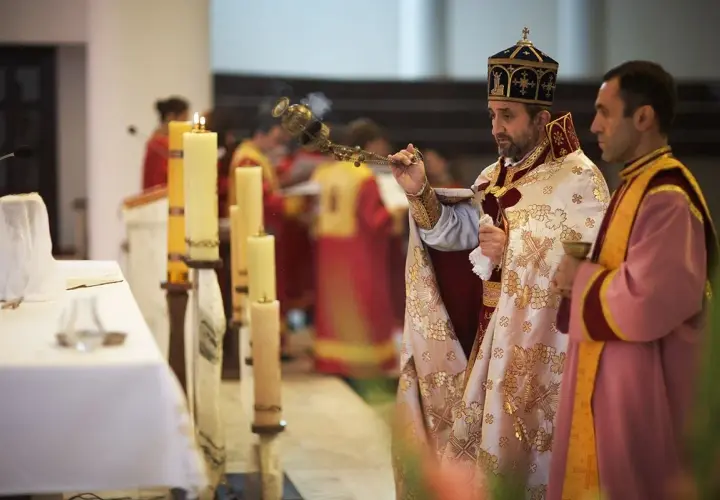 Dwaj duchowni w szatach liturgicznych podczas nabożeństwa, jeden z kadzielnicą, obok świece.