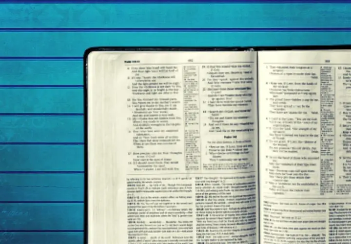 Otwarta Biblia z tekstem w języku angielskim na tle niebieskich desek.
