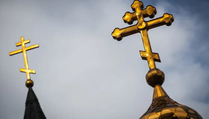 Złoty krzyż prawosławny na tle pochmurnego nieba. Drugi krzyż prawosławny widoczny w oddali.
