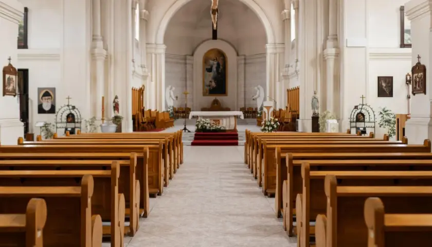 Wnętrze kościoła z rzędami drewnianych ławek. W ołtarzu głównym wisi obraz, a nad nim krucyfiks. 1 maja święto kościelne, czas zadumy.