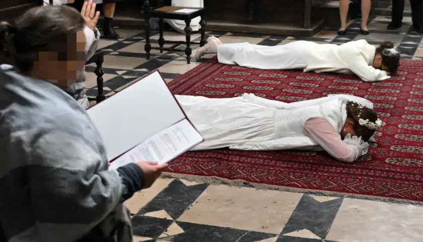 Dwie kobiety w białych sukniach leżą na dywanie w kościele. To uroczystość, podczas której zostają dziewicami konsekrowanymi.