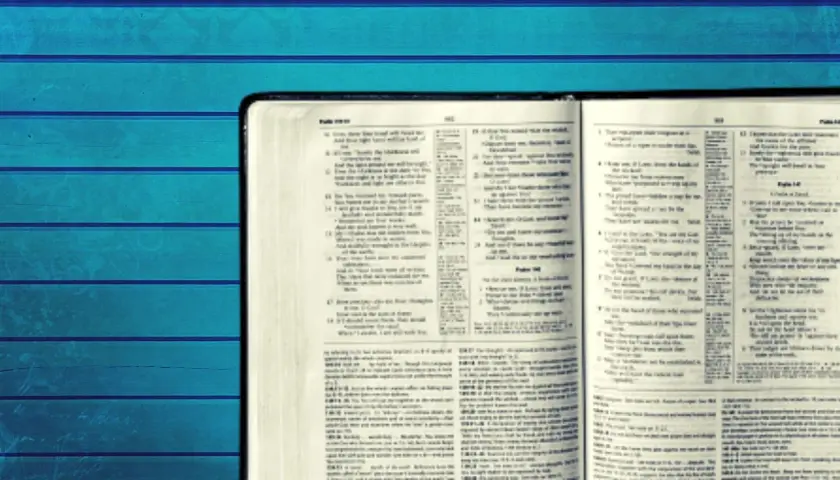 Otwarta Biblia z tekstem w języku angielskim na tle niebieskich desek.