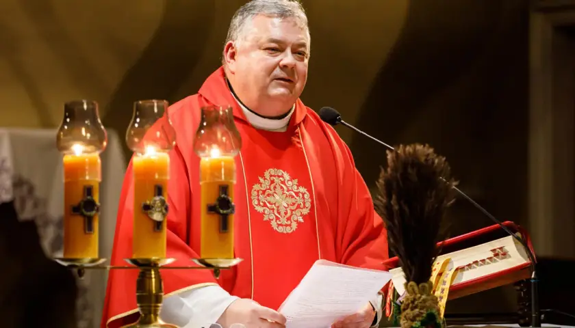 Ksiądz w czerwonej dalmatyce czyta tekst przy świecach. 24 marca, w kościele panuje uroczysta atmosfera.