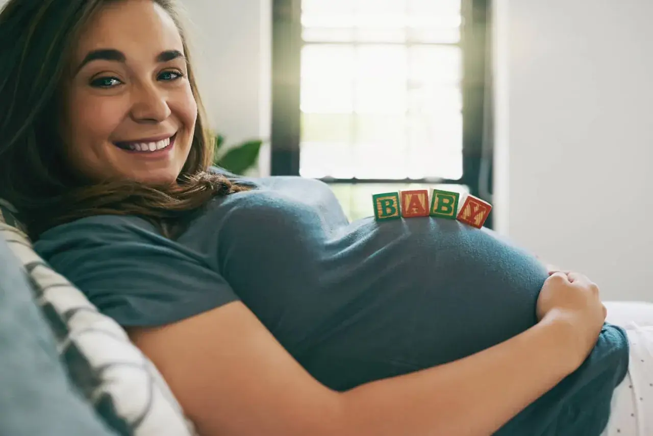 Uśmiechnięta surogatka z klockami "BABY" na brzuchu.