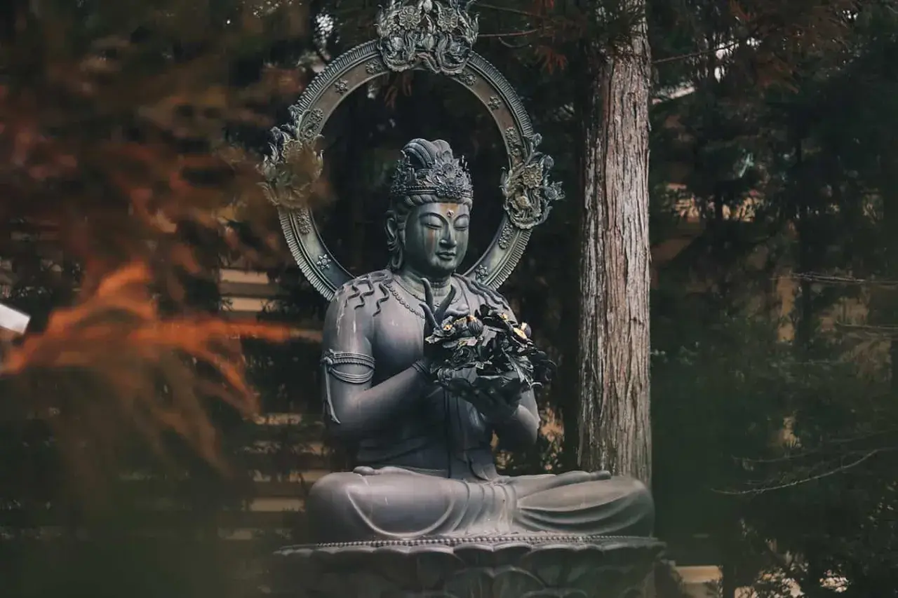 Kamienna statua Buddy w pozycji medytacyjnej, otoczona drzewami. Symbol spokoju i buddyzmu.