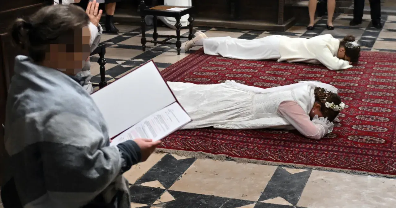 Dwie kobiety w białych sukniach leżą na dywanie w kościele. To uroczystość, podczas której zostają dziewicami konsekrowanymi.
