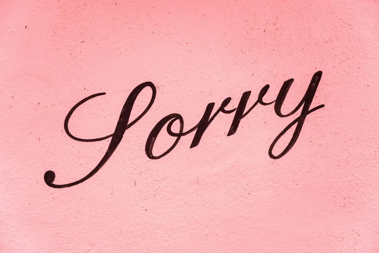 Napis "Sorry" czarną, ozdobną czcionką na różowym, chropowatym tle.