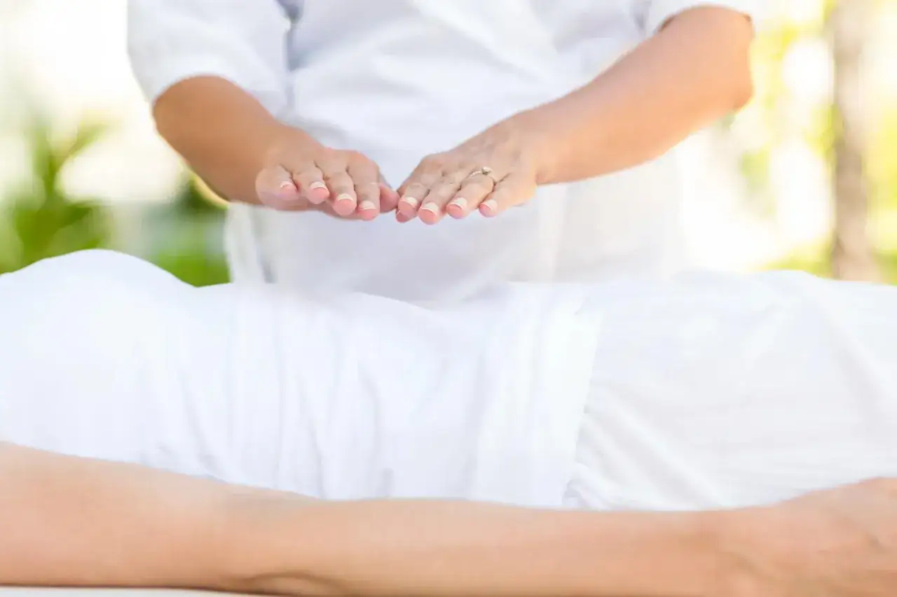 Dłonie terapeuty unoszą się nad ciałem osoby leżącej, przekazując energię reiki.