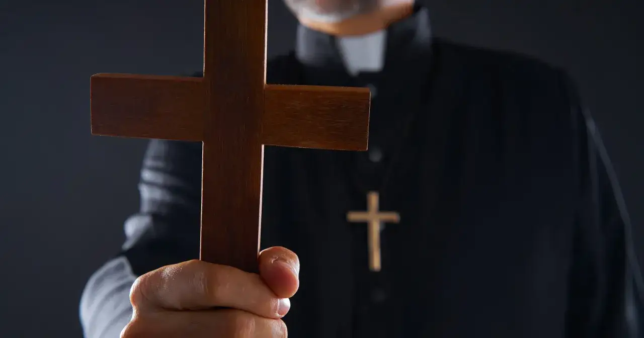 Dłoń księdza trzyma drewniany krzyż, symbol walki z opętaniem.