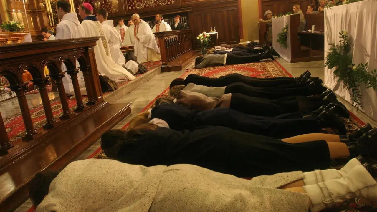 Kobiety leżą krzyżem na dywanie w kościele, podczas ceremonii, która może być ślubowaniem dziewicy konsekrowanej.