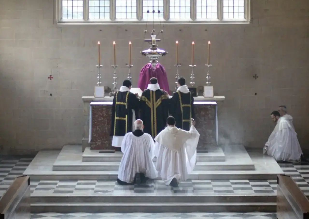 Księża w szatach liturgicznych klęczą przed ołtarzem, otoczeni kadzidłem. W tle płoną świece, a nad nimi wisi ozdobna lampa. Amen.